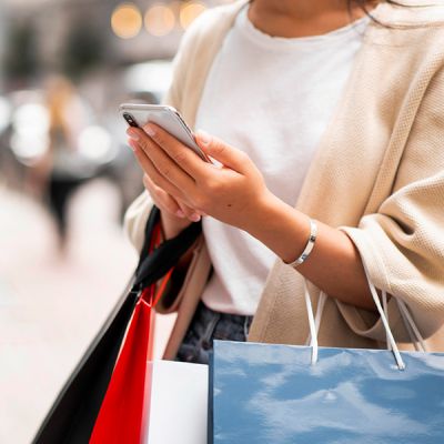 A woman with shopping bags and a cell phone, illustrating the concept of e-commerce and modern online shopping experiences.