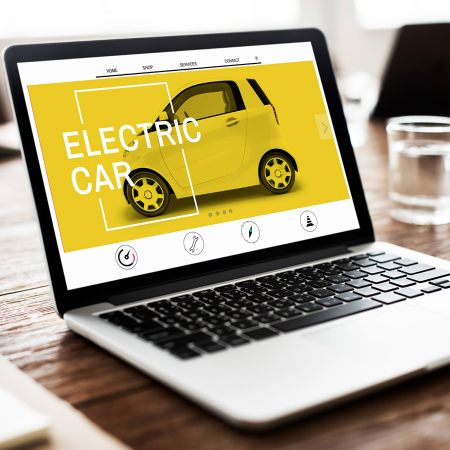 laptop on a table with a small yellow car on the screen with the words Electric Car